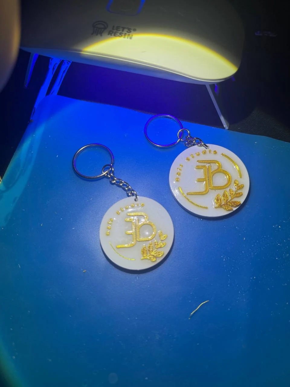 Two white round logo keychains with gold lettering and metal rings
